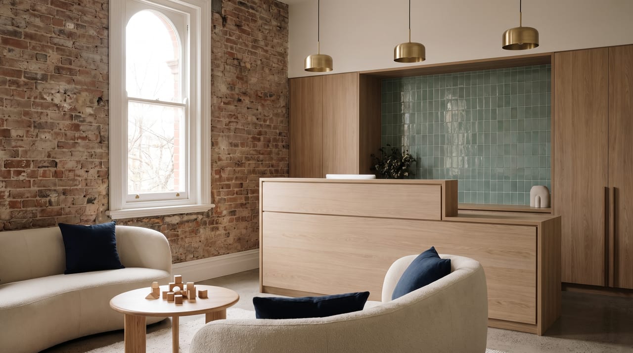 Harborlight's reception: exposed brick, a white oak desk, a low sofa, a small wooden play table and a tall window with daylight